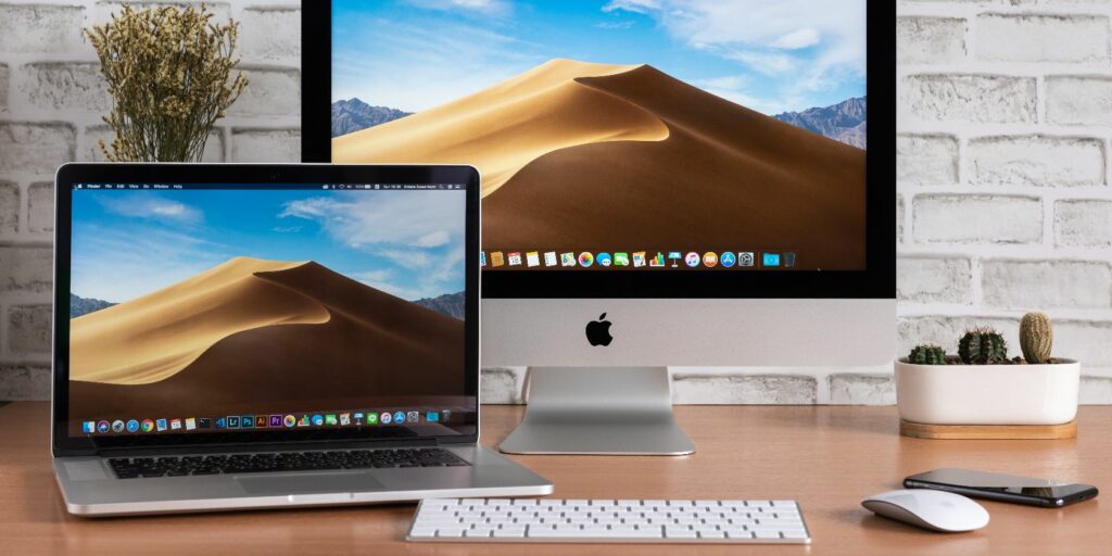 iMac and Macbook computers, keyboard, magic mouse, iPhone and cactus vase on wooden table