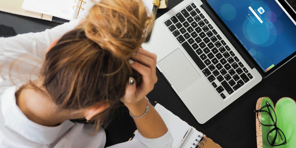 Woman with her head in her hands in front of a MacBook