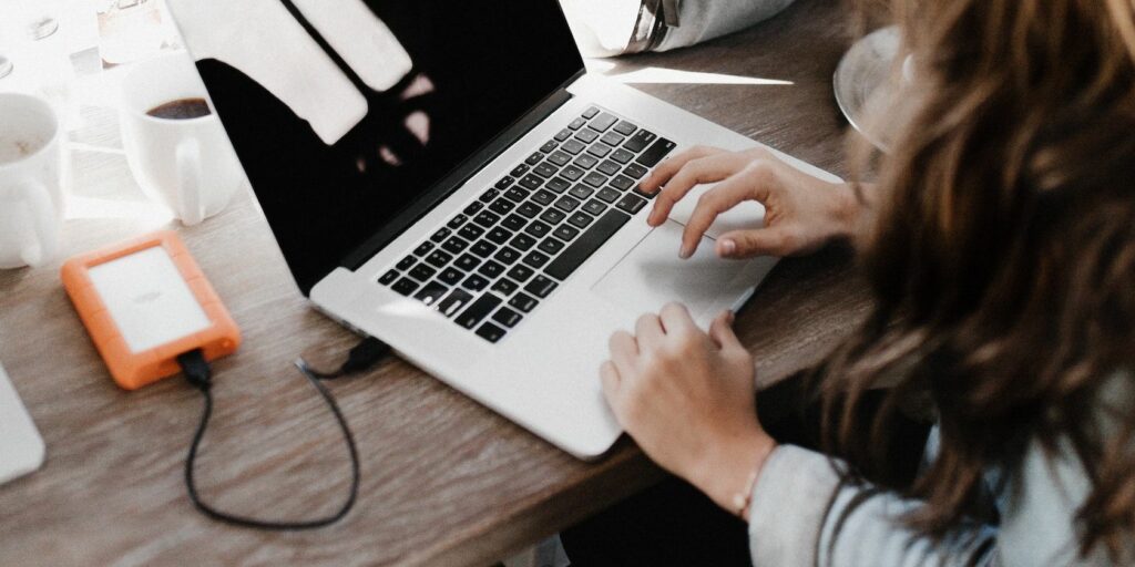 A person uses a MacBook while an external hard drive is plugged into it