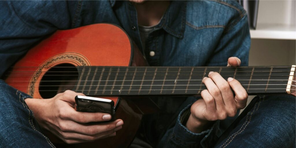 man playing guitar holding phone