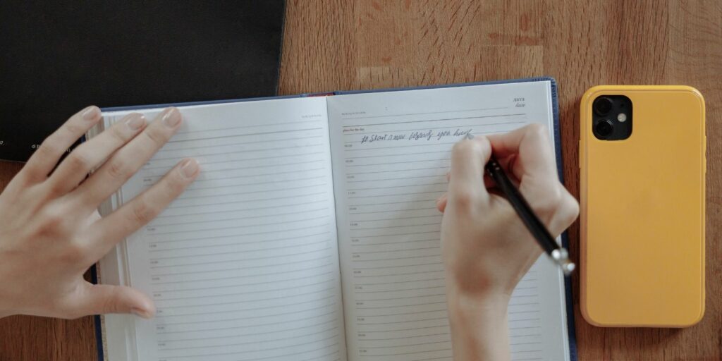 Person Writing Notes with iPhone on the Table