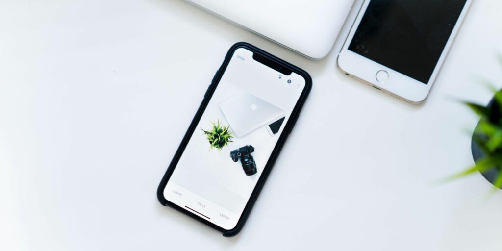 iPhone on a white table top with a photo of a MacBook and camera on it.