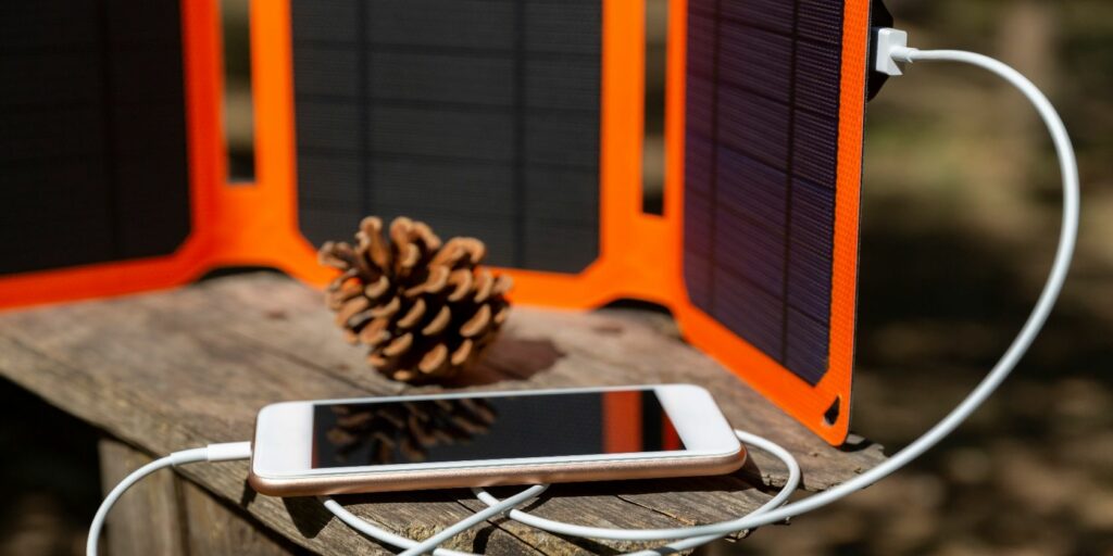 Smartphone is charging from solar battery in summer camp. Clean energy for using in camping.